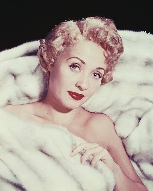 Jane Powell, US actress, dancer and singer, reclining against a white fur surface, covered up to her chest with white fur, circa 1960.
