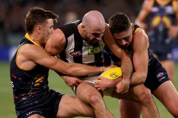 Paul Seedsman and Chayce Jones of the Crows tackle Steele Sidebottom of the Magpies during the 2021 AFL Round 12 match between the Adelaide Crows and...