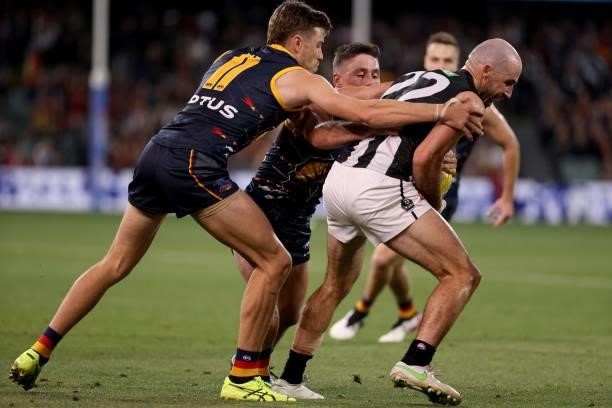 Paul Seedsman and Chayce Jones of the Crows tackle Steele Sidebottom of the Magpies during the 2021 AFL Round 12 match between the Adelaide Crows and...