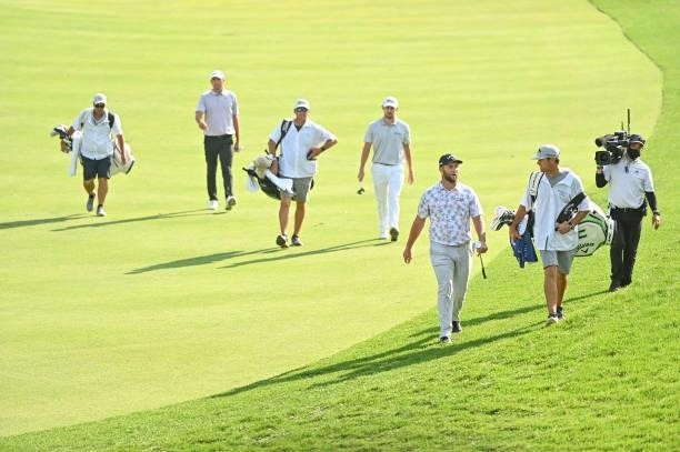 Jon Rahm of Spain, Patrick Cantlay and Scottie Scheffler walk with their caddies along the 17th hole during the third round of the Memorial...