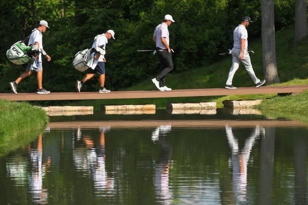 Jon Rahm of Spain and Scottie Scheffler walk with their caddies across a bridge on the 15th hole during the third round of the Memorial Tournament...