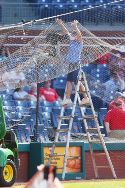 Stadium worker holds up the protective netting after a cable snapped causing the net to collapse from home plate to right field during the eighth...