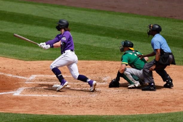 Brendan Rodgers of the Colorado Rockies hits an RBI sacrifice fly as catcher Sean Murphy of the Oakland Athletics and umpire Ramon DeJesus look on...