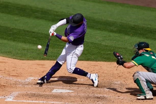 Dom Nunez of the Colorado Rockies hits a sacrifice RBI line drive in the eighth inning against the Oakland Athletics at Coors Field on June 6, 2021...
