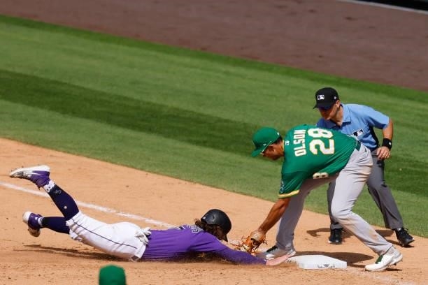 Brendan Rodgers of the Colorado Rockies dives safely back into first base ahead of the throw to Matt Olson of the Oakland Athletics as first base...