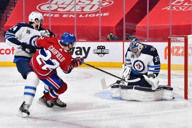 Derek Forbort of the Winnipeg Jets defends against Cole Caufield of the Montreal Canadiens as goaltender Connor Hellebuyck makes a save during the...