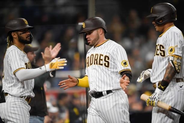 Victor Caratini of the San Diego Padres is congratulated by Fernando Tatis Jr. #23 and Manny Machado after scoring during the second inning of a...