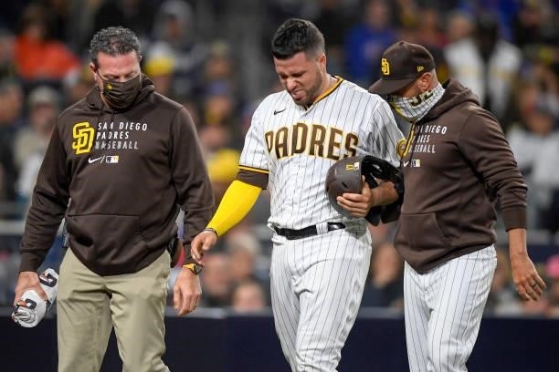 Victor Caratini of the San Diego Padres, center, walks off the field with manager Jayce Tingler, right, and a trainer after scoring during the sixth...