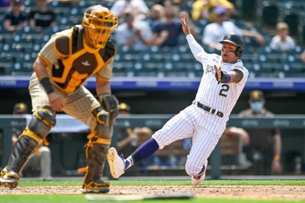Yonathan Daza of the Colorado Rockies slides safely into home base for a run as Webster Rivas of the San Diego Padres waits for the relay throw in...
