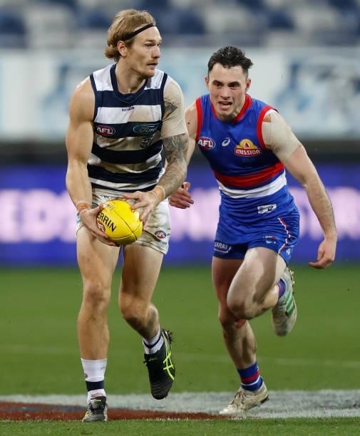 Tom Stewart of the Cats is chased by Toby McLean of the Bulldogs during the 2021 AFL Round 14 match between the Geelong Cats and the Western Bulldogs...