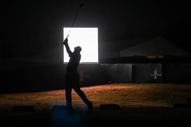 Bryson DeChambeau is silhouetted as he hits balls at night on the practice range after play following the first round of the 121st U.S. Open on the...