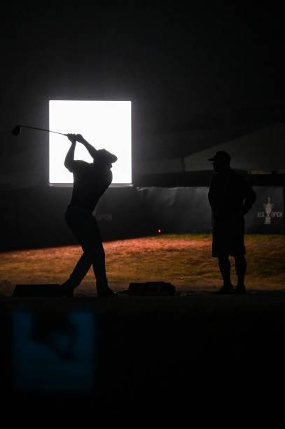 Bryson DeChambeau is silhouetted with caddie Tim Tucker as he hits balls at night on the practice range after play following the first round of the...