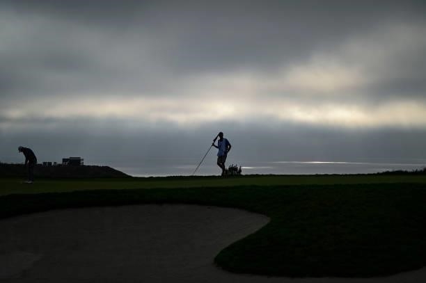 Scenic view of a caddie holding the pin flag on the 14th hole as a marine layer of clouds and fog obscures the sun over the Pacific Ocean during the...
