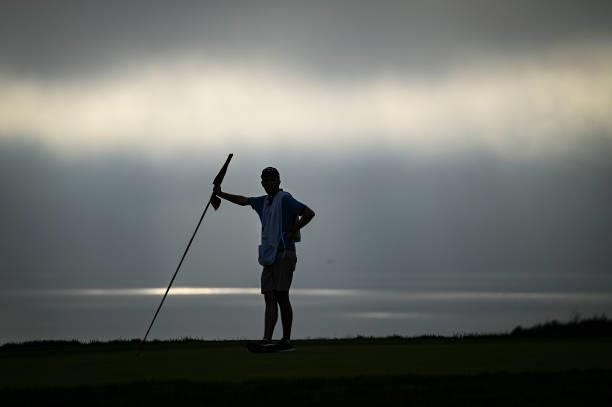 Scenic view of a caddie holding the pin flag on the 14th hole as a marine layer of clouds and fog obscures the sun over the Pacific Ocean during the...