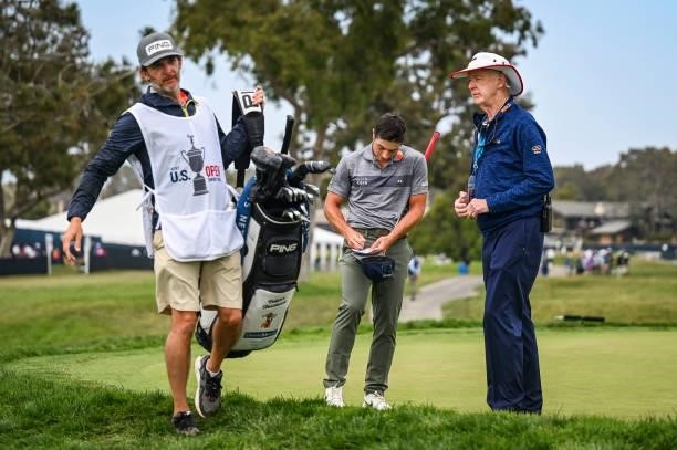 Viktor Hovland signs his scorecard in front of USGA Rules Official Phil Miller after withdrawing from the tournament on the first hole during the...