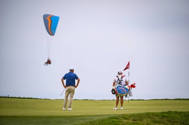 Marc Leishman of Australia and his caddie Matty Kelly stand on the 12th hole green as a paraglider flies by during the third round of the 121st U.S....
