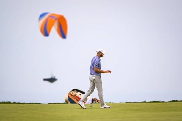 Dustin Johnson waves after making a par putt on the 12th hole green as a paraglider flies by during the third round of the 121st U.S. Open on the...