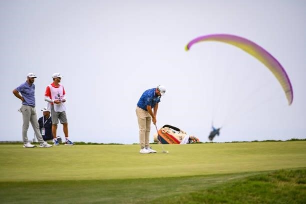 Marc Leishman of Australia putts on the 12th hole green as a paraglider flies by during the third round of the 121st U.S. Open on the South Course at...