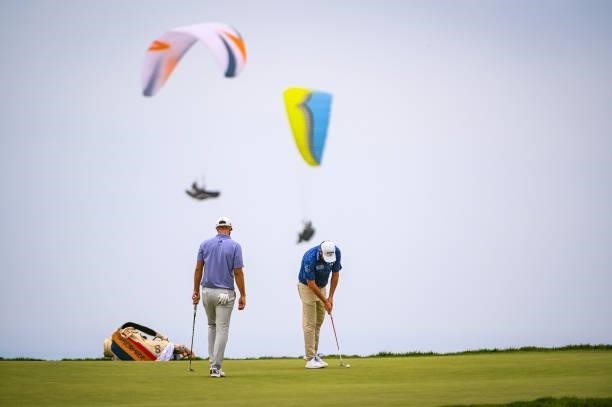 Marc Leishman of Australia putts on the 12th hole green as paragliders fly by during the third round of the 121st U.S. Open on the South Course at...