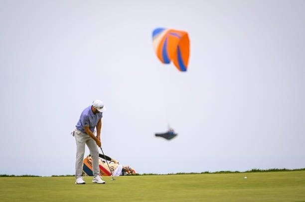 Dustin Johnson makes a putt on the 12th hole green as a paraglider flies by during the third round of the 121st U.S. Open on the South Course at...