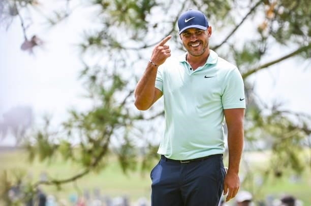 Brooks Koepka smiles and points at his Nike hat after making a birdie putt on the 10th hole green during the third round of the 121st U.S. Open on...