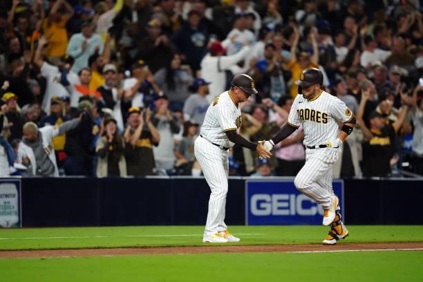 Third base coach Bobby Dickerson of the San Diego Padres high fives Victor Caratini after Caratini hit a home run during the game between the Los...