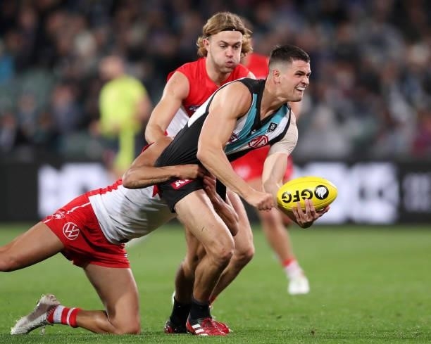 Ryan Burton of the Power tries to break the tackle of James Bell of the Swans and James Rowbottom of the Swans during the 2021 AFL Round 15 match...