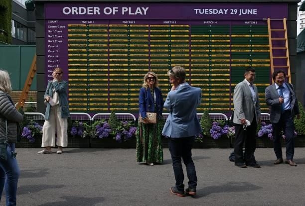 People pose for a photograph in front of the Order of Play board on the second day of the 2021 Wimbledon Championships at The All England Tennis Club...