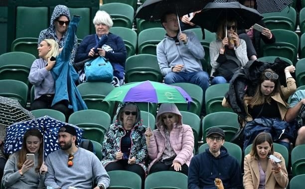 Spectators take cover from the rain on Court 2 during the second day of the 2021 Wimbledon Championships at The All England Tennis Club in Wimbledon,...
