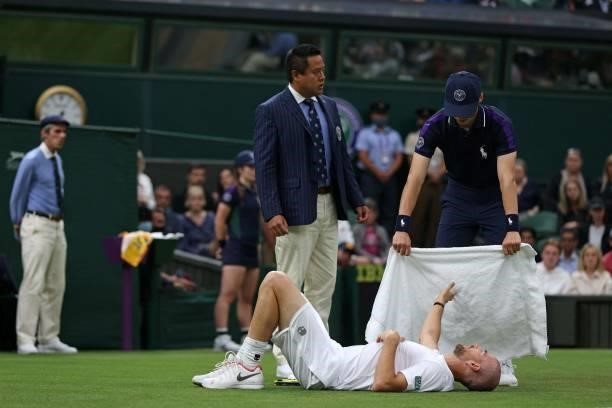 France's Adrian Mannarino holds takes a towel from a ballboy after slipping on the grass during play against Switzerland's Roger Federer during their...