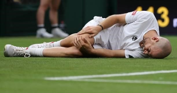 France's Adrian Mannarino holds his knee after slipping on the grass during play against Switzerland's Roger Federer during their men's singles first...