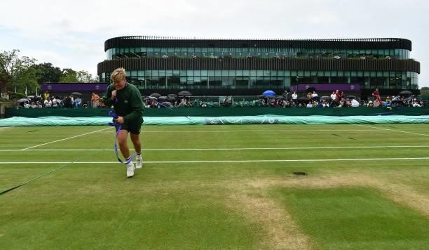 Ground staff pull on the court covers as rain stops play on the sixth day of the 2021 Wimbledon Championships at The All England Tennis Club in...