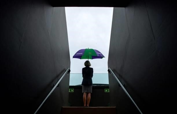 Steward shelter from the rain beneath an umbrella as rain stops play on Court 3 on the sixth day of the 2021 Wimbledon Championships at The All...