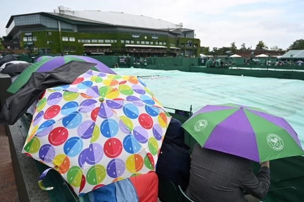 Spectators hide beneath umbreallas on court 8 as rain stops play on the sixth day of the 2021 Wimbledon Championships at The All England Tennis Club...