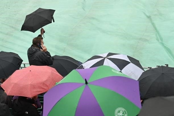 Spectators hide beneath umbreallas on court 12 as rain stops play on the sixth day of the 2021 Wimbledon Championships at The All England Tennis Club...