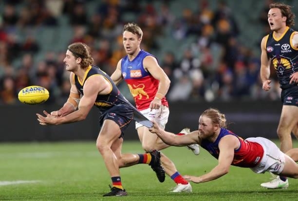 Sam Berry of the Crows handpasses the ball while Daniel Rich of the Lions tries to stop him during the 2021 AFL Round 16 match between the Adelaide...