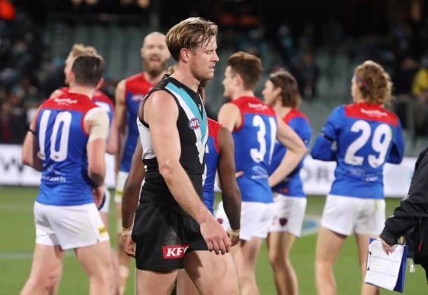 Port Captain, Tom Jonas walks off the oval with Melbourne players celebrating in the background during the 2021 AFL Round 17 match between the Port...