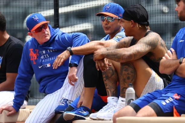 Manager Luis Rojas of the New York Mets sits between bench coach Dave Jauss and pitcher Marcus Stroman as they watch Carlos Carrasco throw off the...