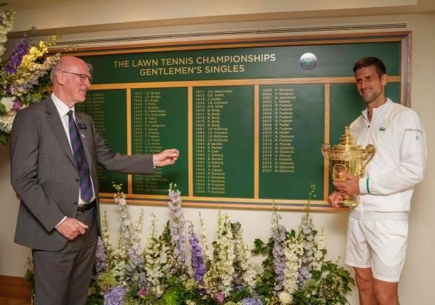 Serbia's Novak Djokovic holds the winner's trophy as he stands with Ian Hewitt, AELTC Chairman, in front of the honours board after defeating Italy's...