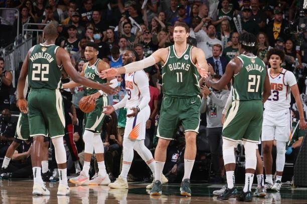 Brook Lopez hi-fives Khris Middleton and Jrue Holiday of the Milwaukee Bucks during Game Three of the 2021 NBA Finals on July 11, 2021 at the Fiserv...