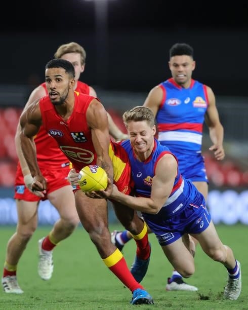 Touk Miller of the Suns releases the ball as he is tackled by Lachie Hunter of the Bulldogs during the 2021 AFL Round 18 match between the Gold Coast...