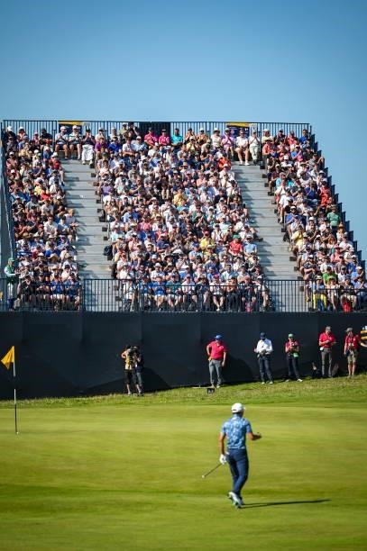 Collin Morikawa chips a shot to the seventh hole green as fans applaud from a grandstand during Day Four of the 149th The Open Championship at Royal...