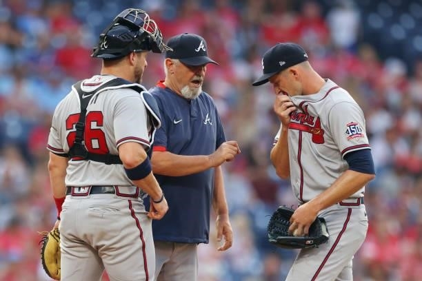 Pitcher Drew Smyly of the Atlanta Braves wipes his face as he listens to pitching coach Rick Kranitz and catcher Stephen Vogt during the third inning...