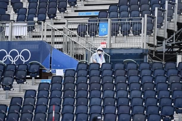 An attendant wearing a poncho sits amid empty stands during the women's preliminary beach volleyball pool B match between the USA and Spain during...