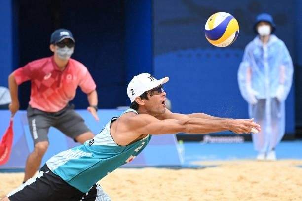 Japan's Katsuhiro Shiratori reaches for the ball, as a linesman and attendant watch, in their men's preliminary beach volleyball pool F match between...