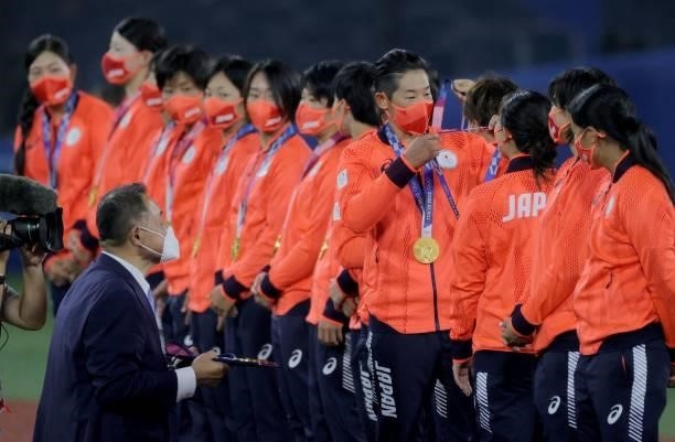 Japan's softball player Yukiko Ueno puts the gold medal to catcher Haruka Agatsuma on the podium with other teammates while medal presenter Japan...