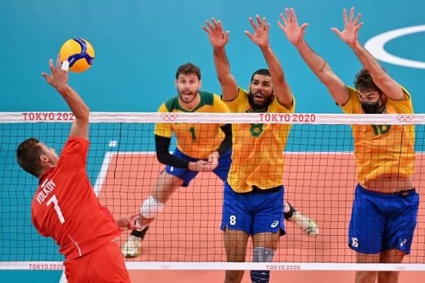 Russia's Dmitry Volkov hits the ball in front of Brazil's Wallace de Souza and Lucas Saatkamp in the men's preliminary round pool B volleyball match...
