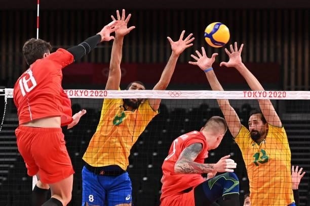Russia's Egor Kliuka spikes the ball past Brazil's Wallace de Souza and Mauricio de Souza in the men's preliminary round pool B volleyball match...