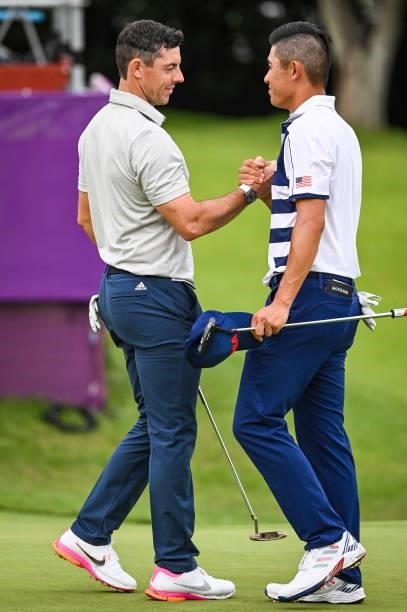Rory McIlroy of Team Ireland shakes hands with Collin Morikawa of Team USA on the 18th hole following the first round of Mens Individual Stroke Play...
