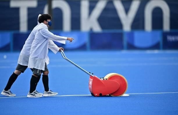 Volunteers prepare the pitch after heavy rain delayed the women's pool A match of the Tokyo 2020 Olympic Games field hockey competition between South...